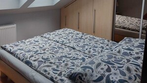 Een slaapkamer met dakraam, een bed met decoratieve beddengoed, houten kasten en een garderobe met spiegel.