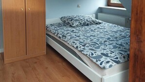 A bedroom with a wooden wardrobe, a bed with patterned bedding, and a radiator.