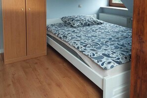 Une chambre avec une armoire en bois, un lit avec une literie à motifs et un radiateur.