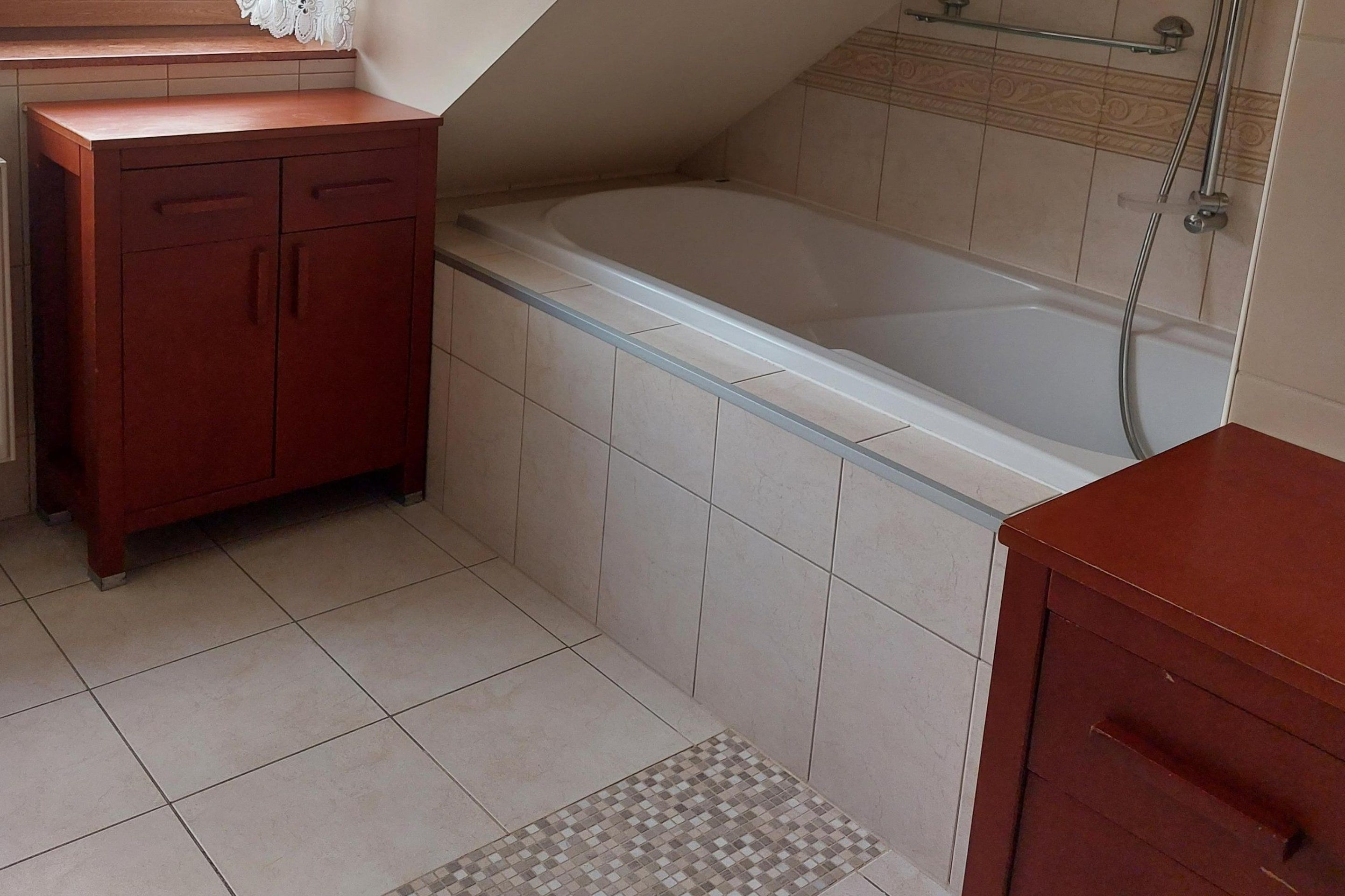 Ein Badezimmer mit einer Badewanne, einem Holzschrank und Fliesenwänden.