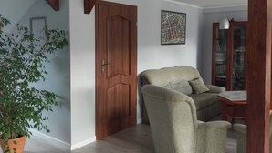 Een ruime woonkamer met een houten deur, een bank, een bijzettafeltje en een plant in pot.