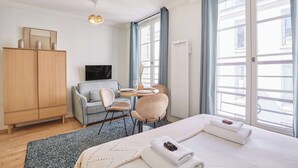 A hotel room with a bed, a TV, a desk with chairs, a wardrobe, and large windows. - Superb Studio Center of Paris Montorgueil (Paris)