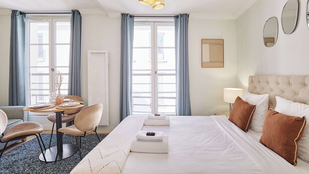 A hotel room with a bed, a round dining table with chairs, a lamp, and a window with curtains. - Superb Studio Center of Paris Montorgueil (Paris)