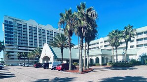 A hotel with a modern design, featuring a large parking area and palm trees. - Coastal Waves Ocean View Studio condo (Daytona Beach)