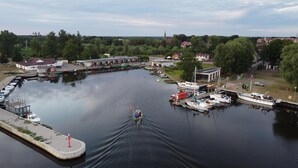 A marina with boats docked, a small building with a red roof, and a church in the background. - Holiday Home in Stepnica Near Szczecin Lagoon (Stepnica)