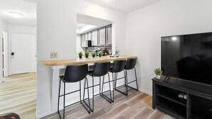 A modern kitchen with a bar area, a flat-screen TV, and a door leading to another room.