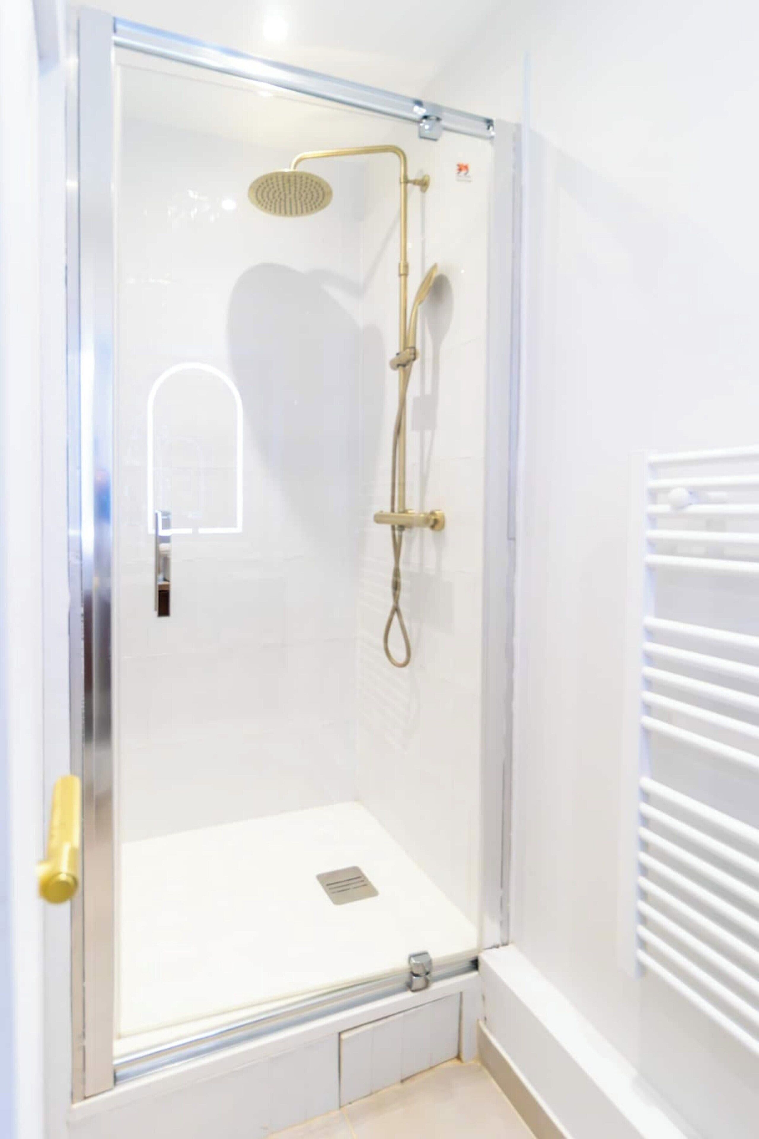 Ducha con cerramiento de vidrio, cabezal de ducha dorado y ducha de mano.