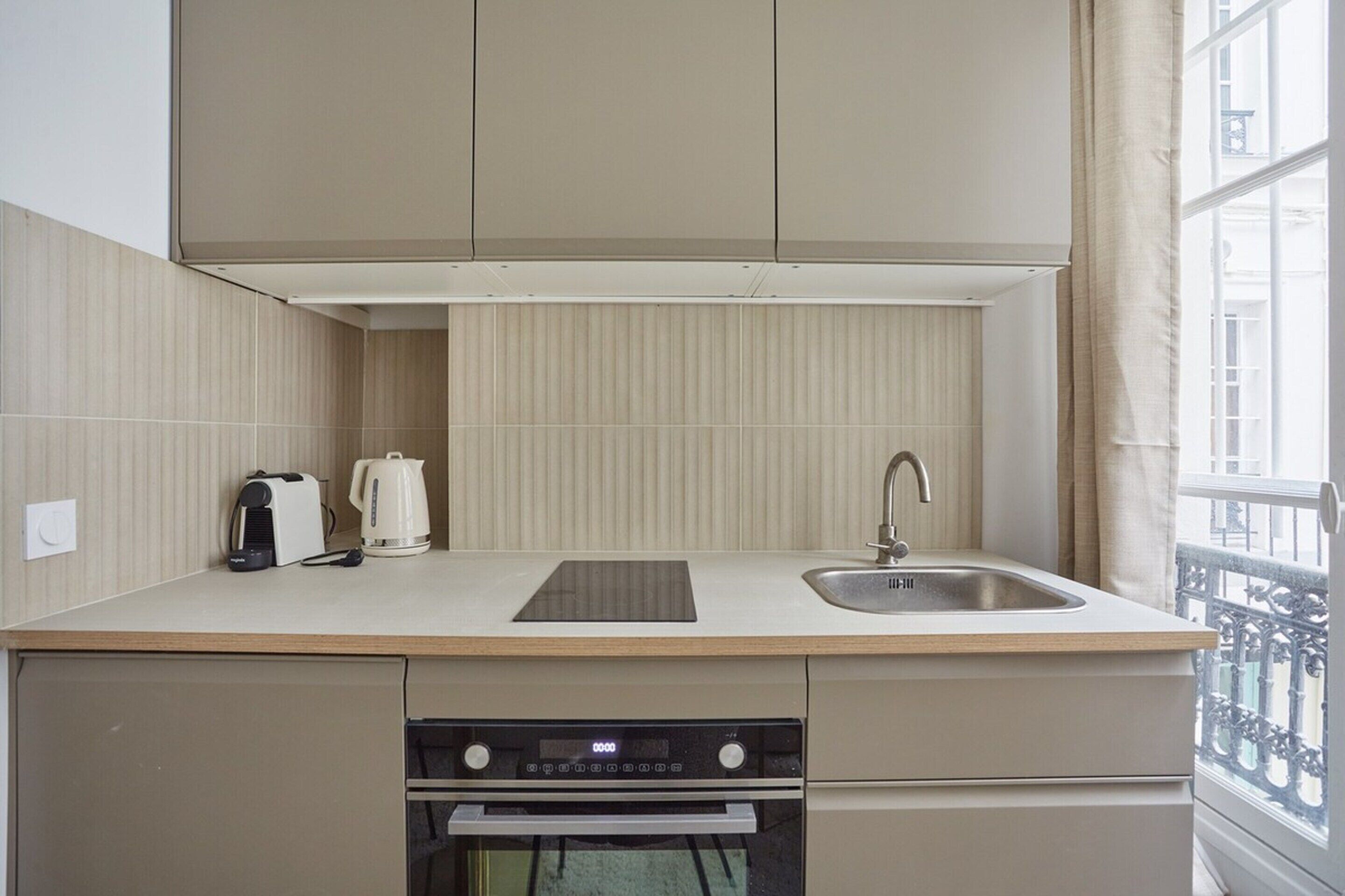 A compact kitchen with a built-in oven, a sink, and a window with a view.
