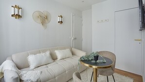 A modern living room with a beige sofa, a round table with a plant, and wall-mounted light fixtures. - Charming Studio - Le Marais - Bastille (Paris)