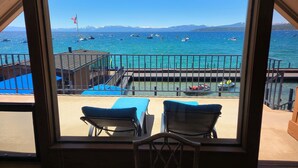 Un balcón con dos sillones de descanso frente a un puerto deportivo con barcos y montañas al fondo.