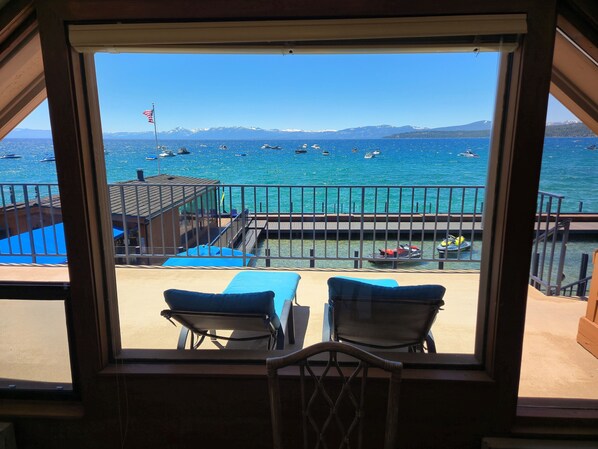 A balcony with two lounge chairs facing a marina with boats and a mountainous backdrop.