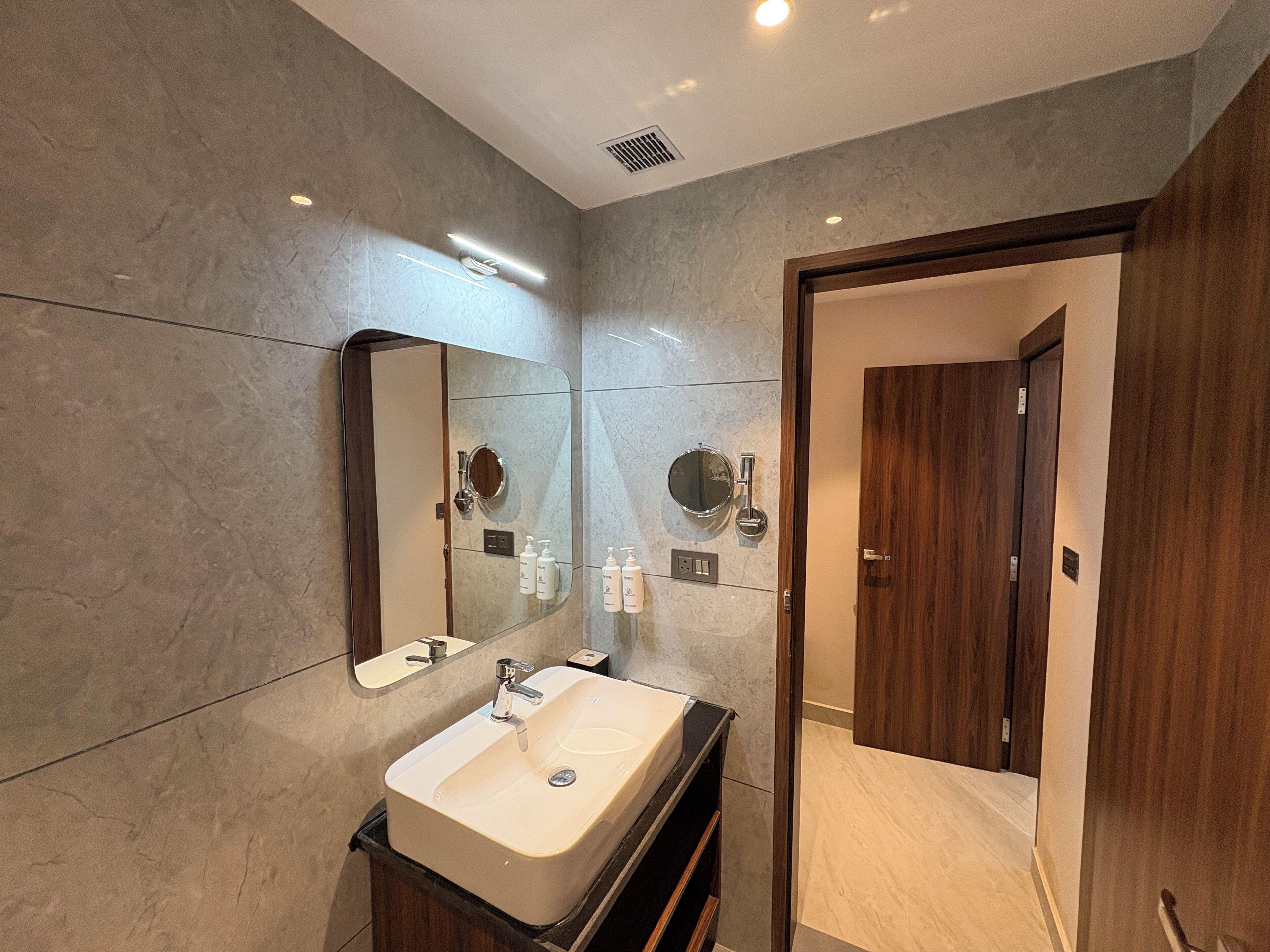 A modern bathroom with a large mirror, a sink, and a wooden door.