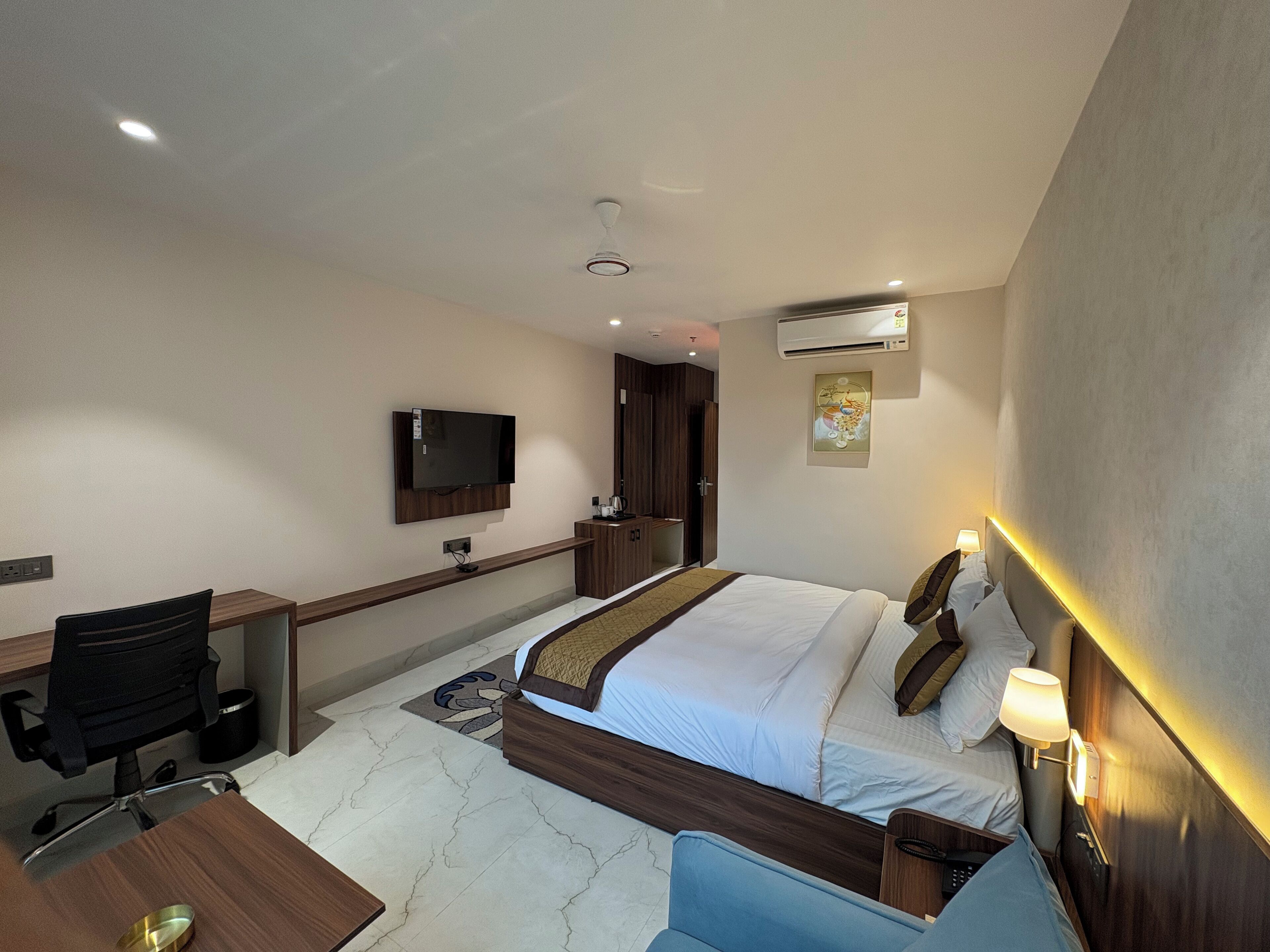 A hotel room with a bed, desk, chair, TV, and artwork on the wall.