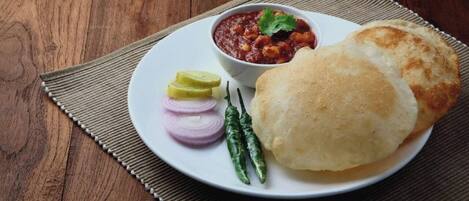Une assiette avec un petit pain, un bol de sauce, des oignons en tranches et des piments verts.