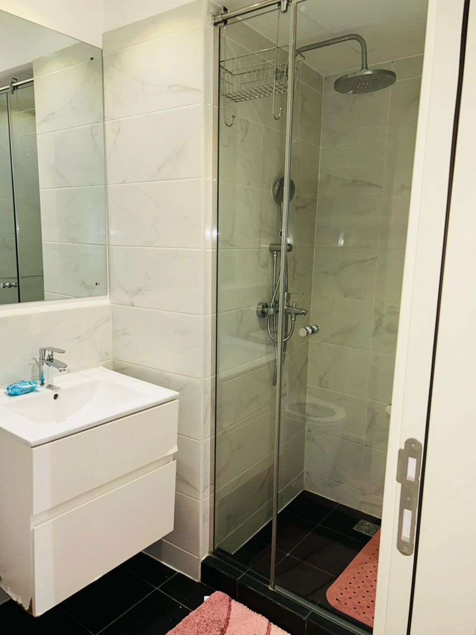 Un baño con ducha acristalada, un lavabo blanco y un espejo.
