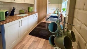 Eine kleine Küche mit weißen Schränken, einer Holz Arbeitsplatte, einer eingebauten Mikrowelle und einer Kaffeemaschine.