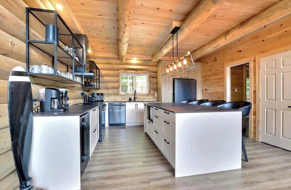 A modern kitchen with wooden walls, a central island, and a coffee machine. - Spa, Game Room, Absolute Comfort | Le Commandant (Saint-Philémon)