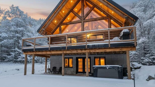A log cabin with a balcony, wooden deck, and a covered outdoor seating area. - Spa, Game Room, Absolute Comfort | Le Commandant (Saint-Philémon)