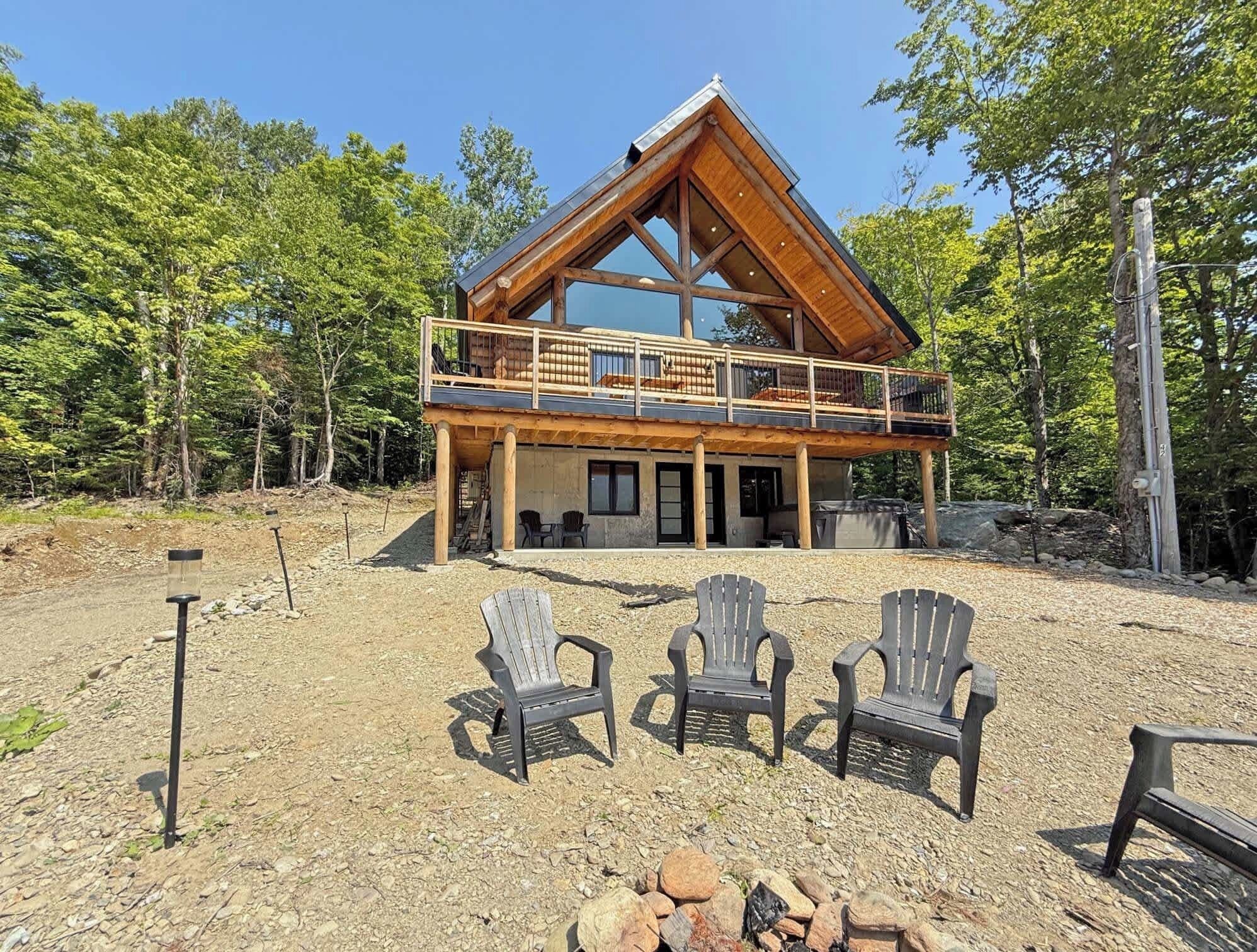 Een chalet met houten gevel, een balkon en een vuurplaats met stoelen.