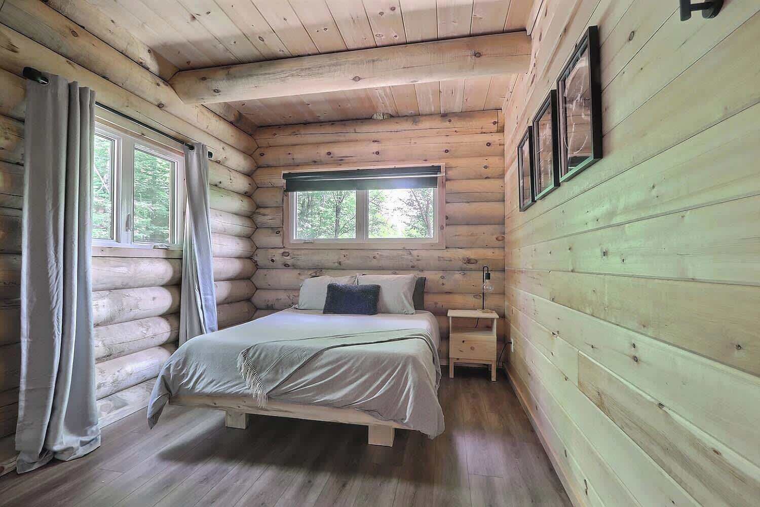 Un dormitorio tipo cabaña de madera con cama, mesita de noche y ventana.