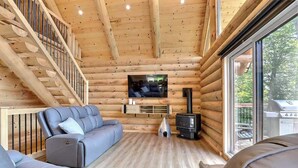 A log cabin interior with a sofa, TV, and fireplace. - Spa, Game Room, Absolute Comfort | Le Commandant (Saint-Philémon)