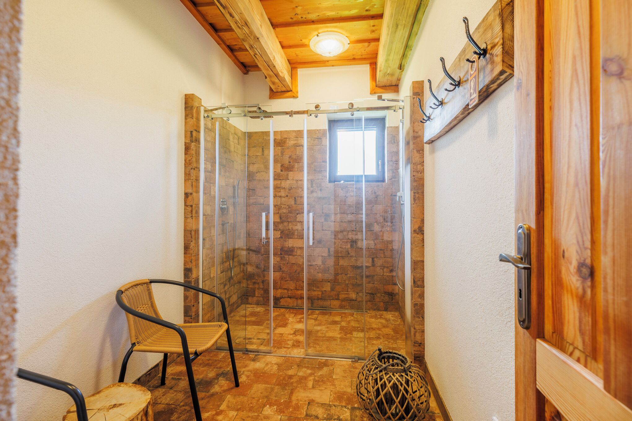 Un angolo doccia con porta in vetro, una sedia in vimini e una porta in legno con ganci.