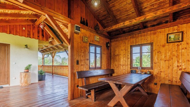 A wooden cabin interior with a wooden deck, benches, a picnic table, and two windows.