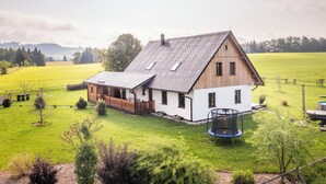 A two-story house with a sloped roof, a wooden deck, and a trampoline in the yard.