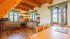 A modern kitchen with wooden cabinets, a wooden dining table, and a view of the outdoors through large windows.