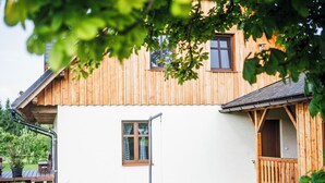 A wooden house with a white exterior, a porch, and a small garden area with a stone wall and a wooden bench.