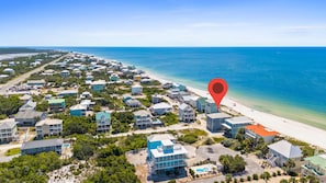 Vista aérea de uma área residencial costeira com casas, uma praia e oceano azul cristalino.
