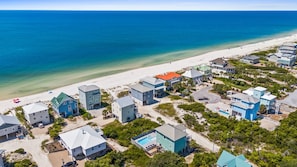 Vista aérea de uma área residencial costeira com casas, praia e oceano azul claro.