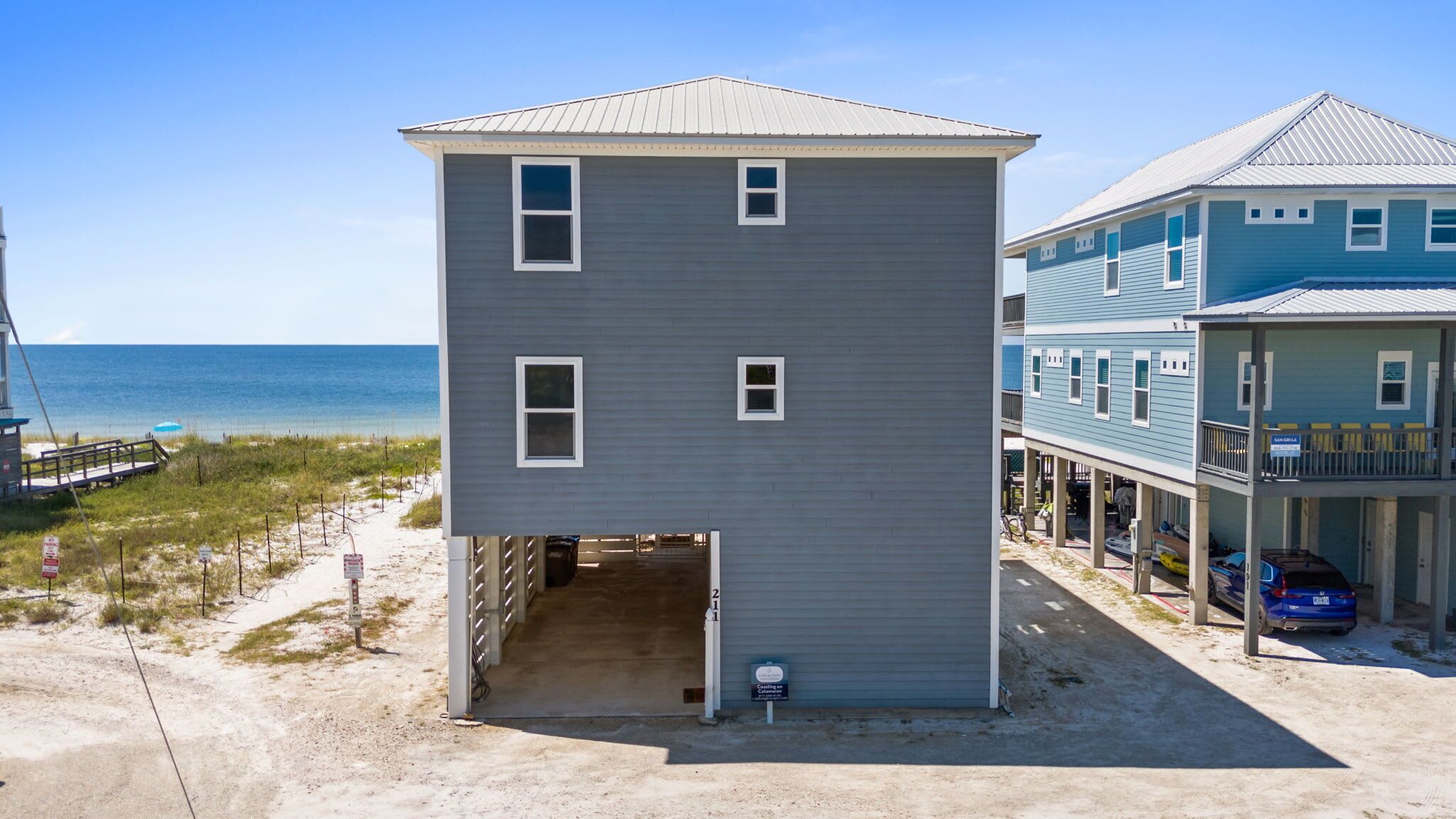 A two-story building with a covered entrance, a beach view, and a parking area with a blue car.