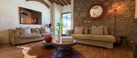 Un salon avec deux canapés, une table basse ronde, un mur en pierre et un grand miroir.