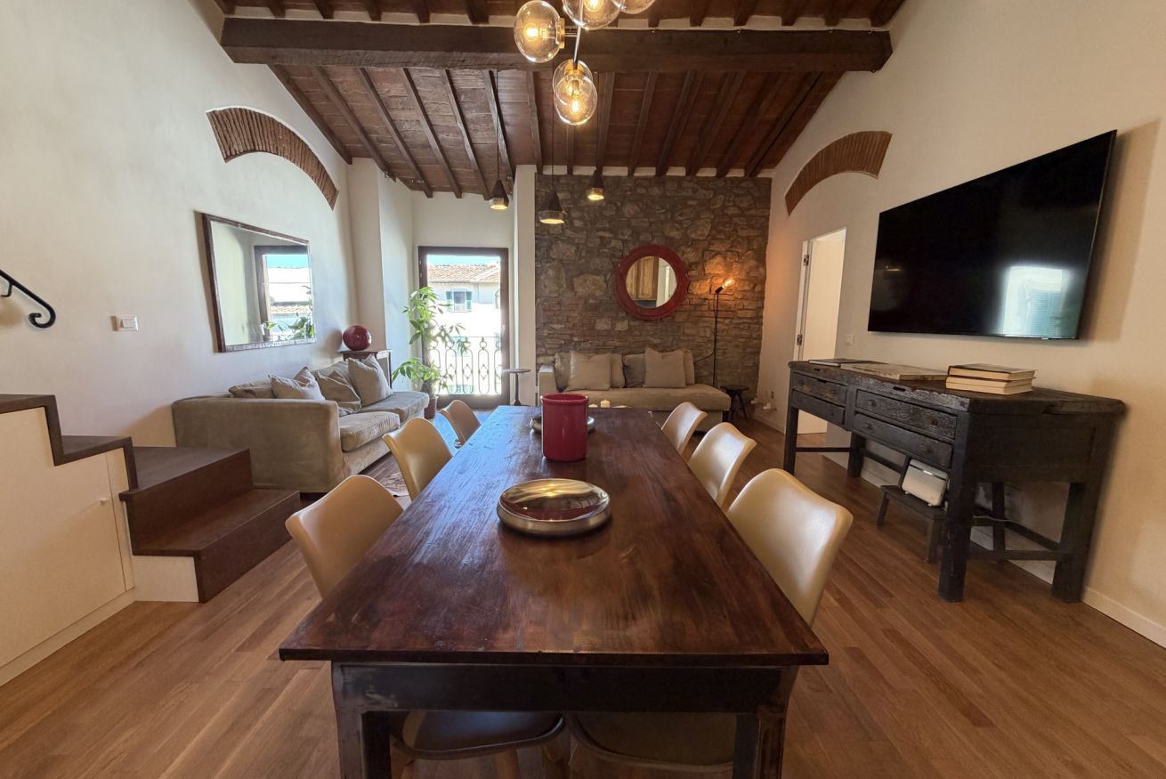 Uma sala de jantar com uma mesa de madeira, cadeiras e uma TV fixada na parede.