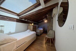 Une chambre avec une lucarne, des poutres en bois, un lit, une chaise et un mur en pierre.