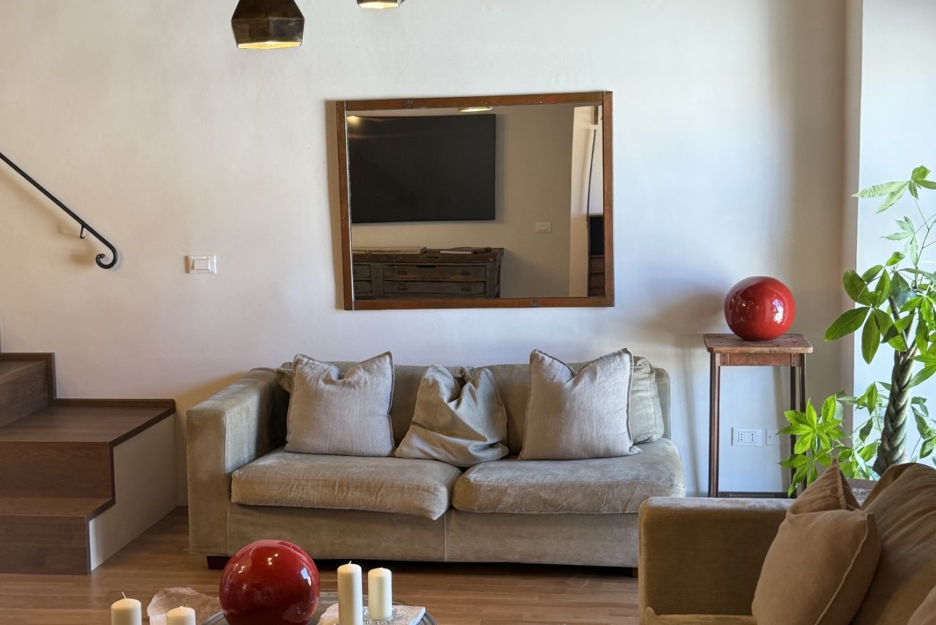 Una sala de estar con un sofá, un objeto esférico rojo y un espejo en la pared.