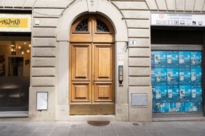 Une porte à deux battants en bois, surmontée d’une petite fenêtre, intégrée à un bâtiment dont la façade présente un relief particulier.