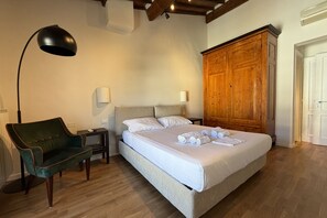 Een slaapkamer met een bed, een groene fauteuil, een houten garderobe en een vloerlamp.
