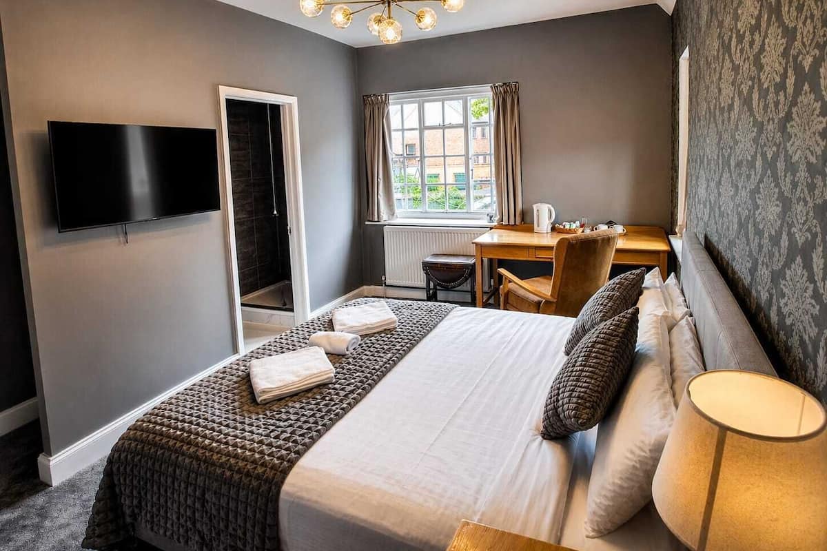 Quarto de hotel com cama, escrivaninha, cadeira, televisão e janela com cortinas.