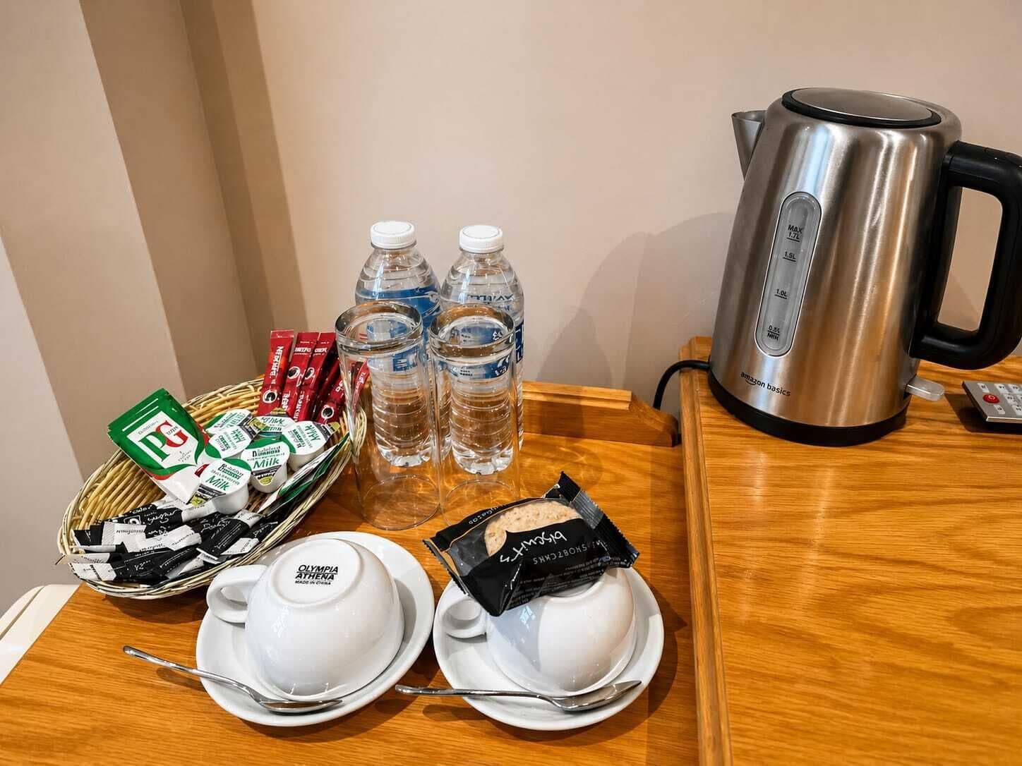 Una disposición para el desayuno con una tetera, botellas de agua, una cesta de aperitivos y dos tazones de yogur.