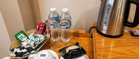 Una disposición para el desayuno con una tetera, botellas de agua, una cesta de aperitivos y dos tazones de yogur.