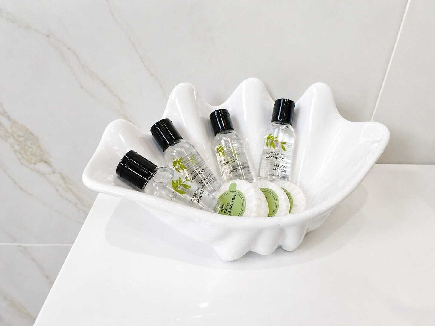 A white ceramic dish containing several clear bottles with black caps, some with green leaf designs, placed on a white surface.