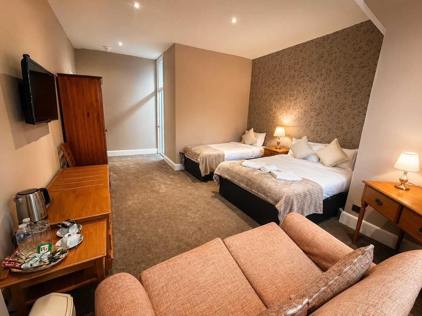 A hotel room with two beds, a TV, a dining area with a table and chairs, and a sofa.