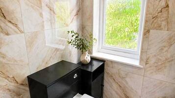 A bathroom with marble walls, a black vanity, a toilet, and a window with a view of greenery.