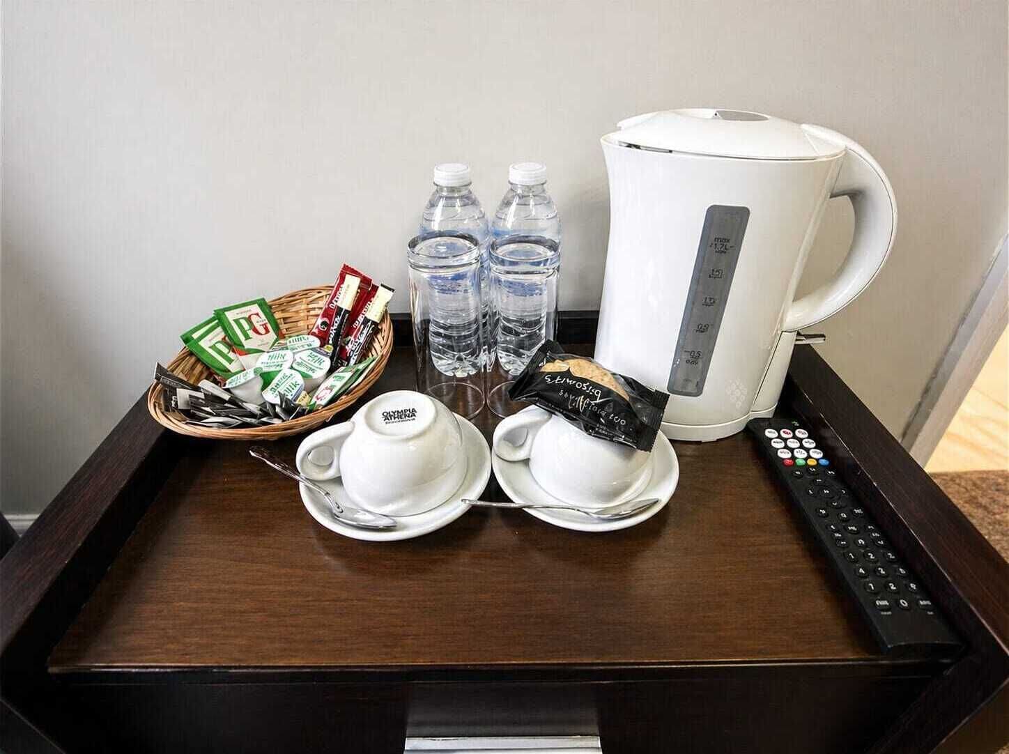 A tray with a coffee maker, water bottles, a basket of snacks, and a remote control.