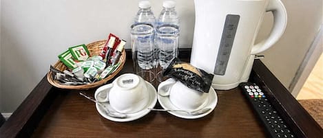 A tray with a coffee maker, water bottles, a basket of snacks, and a remote control.