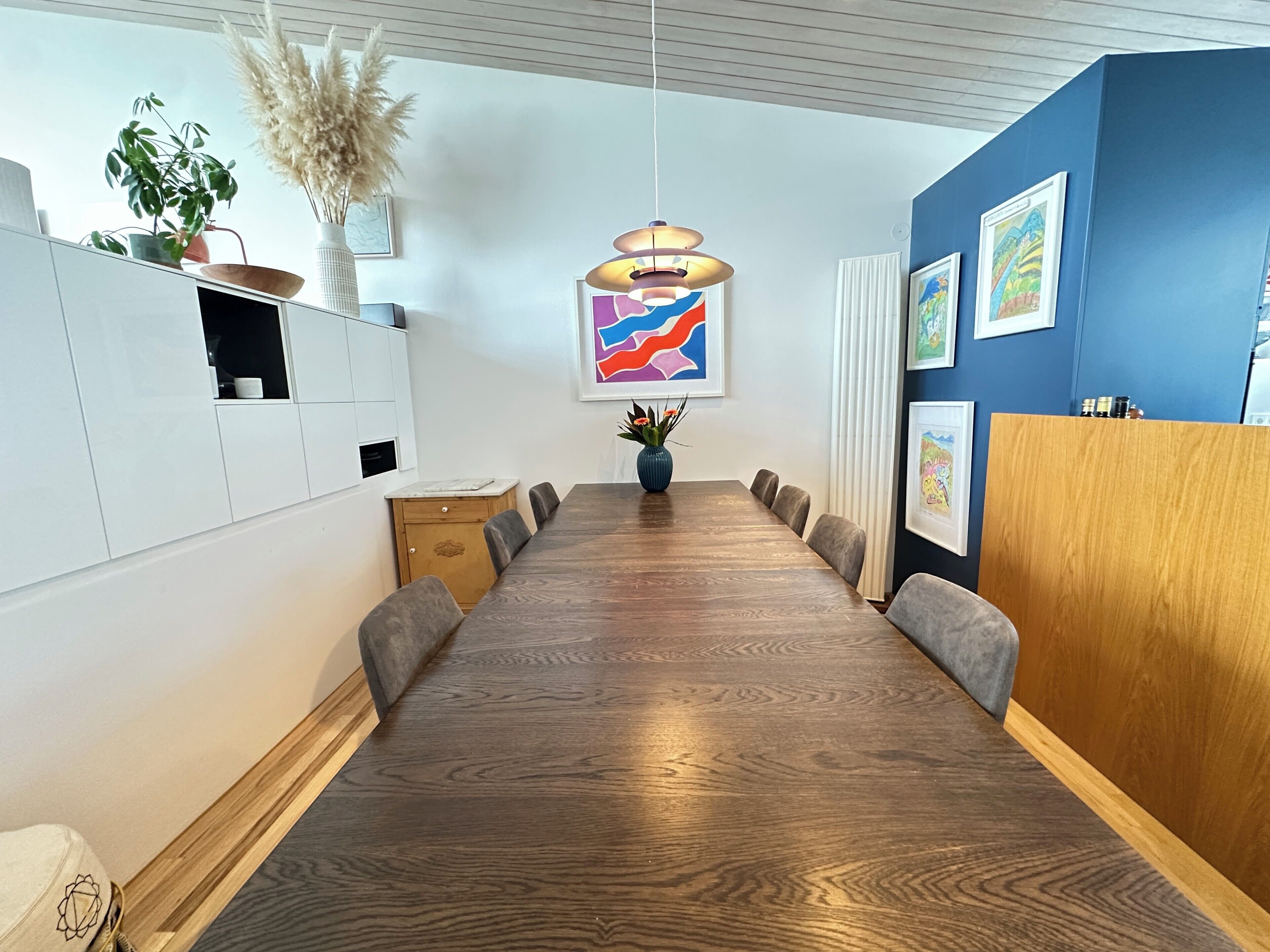Une salle de conférence moderne avec une longue table en bois, des chaises grises, un mur d’accent bleu et un luminaire suspendu.