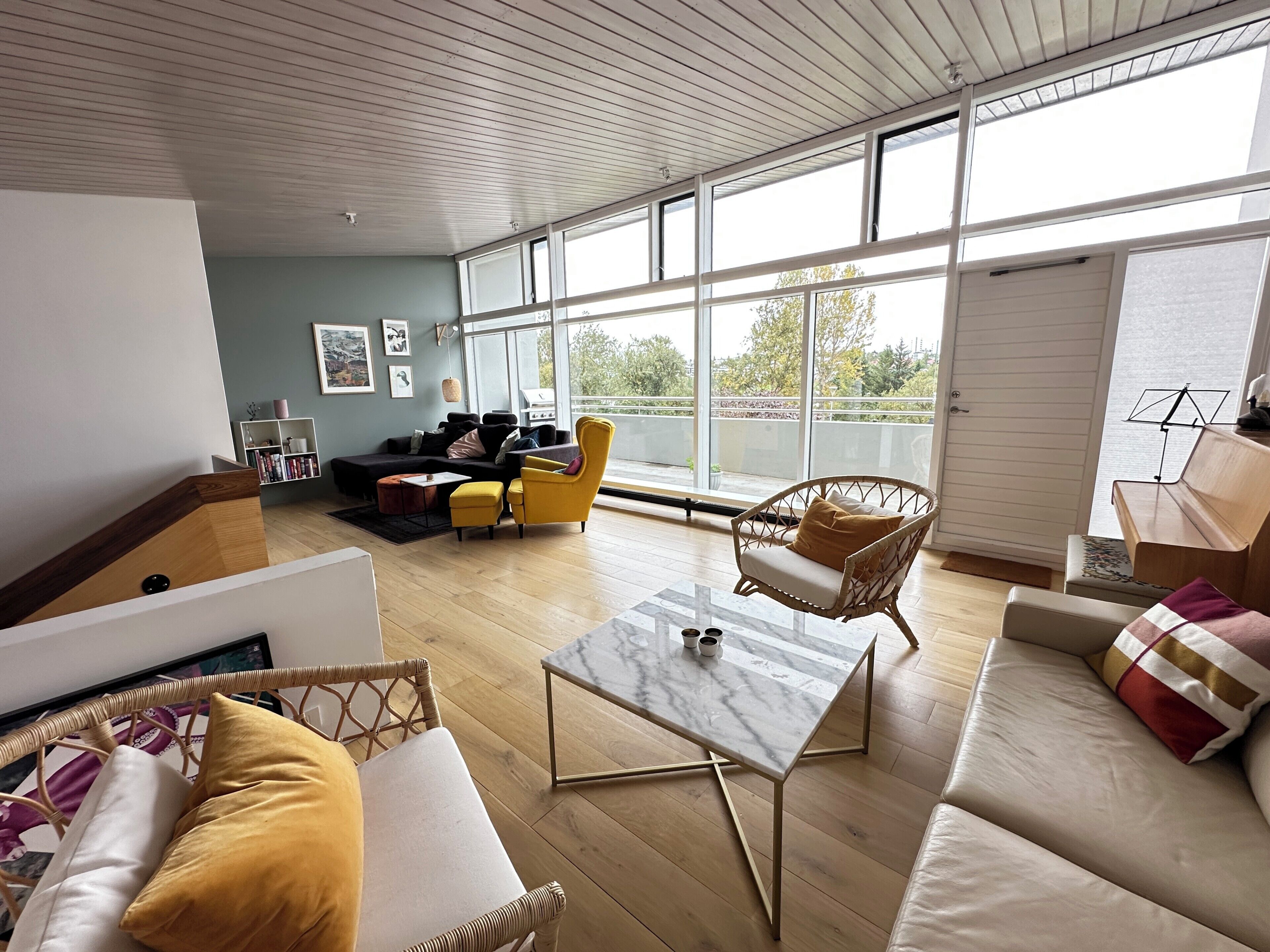 Un salon spacieux avec une grande fenêtre, un canapé, une table basse et un fauteuil en osier.