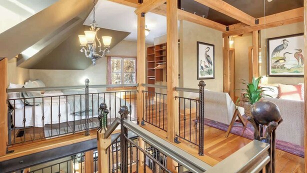 A spacious loft bedroom with a high ceiling, wooden beams, a mezzanine level, a chandelier, and artwork on the walls. - US Bank | Downtown Mpls | Convention Center (Minneapolis)